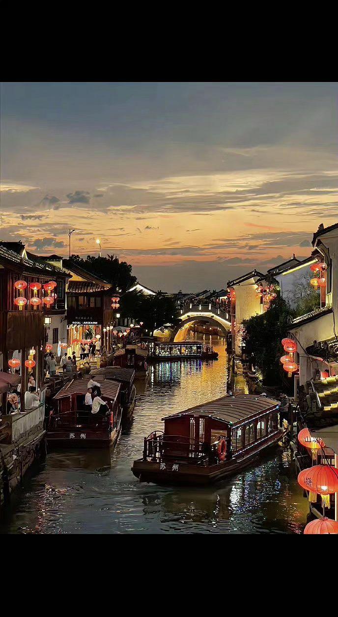 🌆灯笼在暮色里醒着，船影是流动的诗行✨。水面揉碎了晚霞，千年古镇正把故事讲给晚