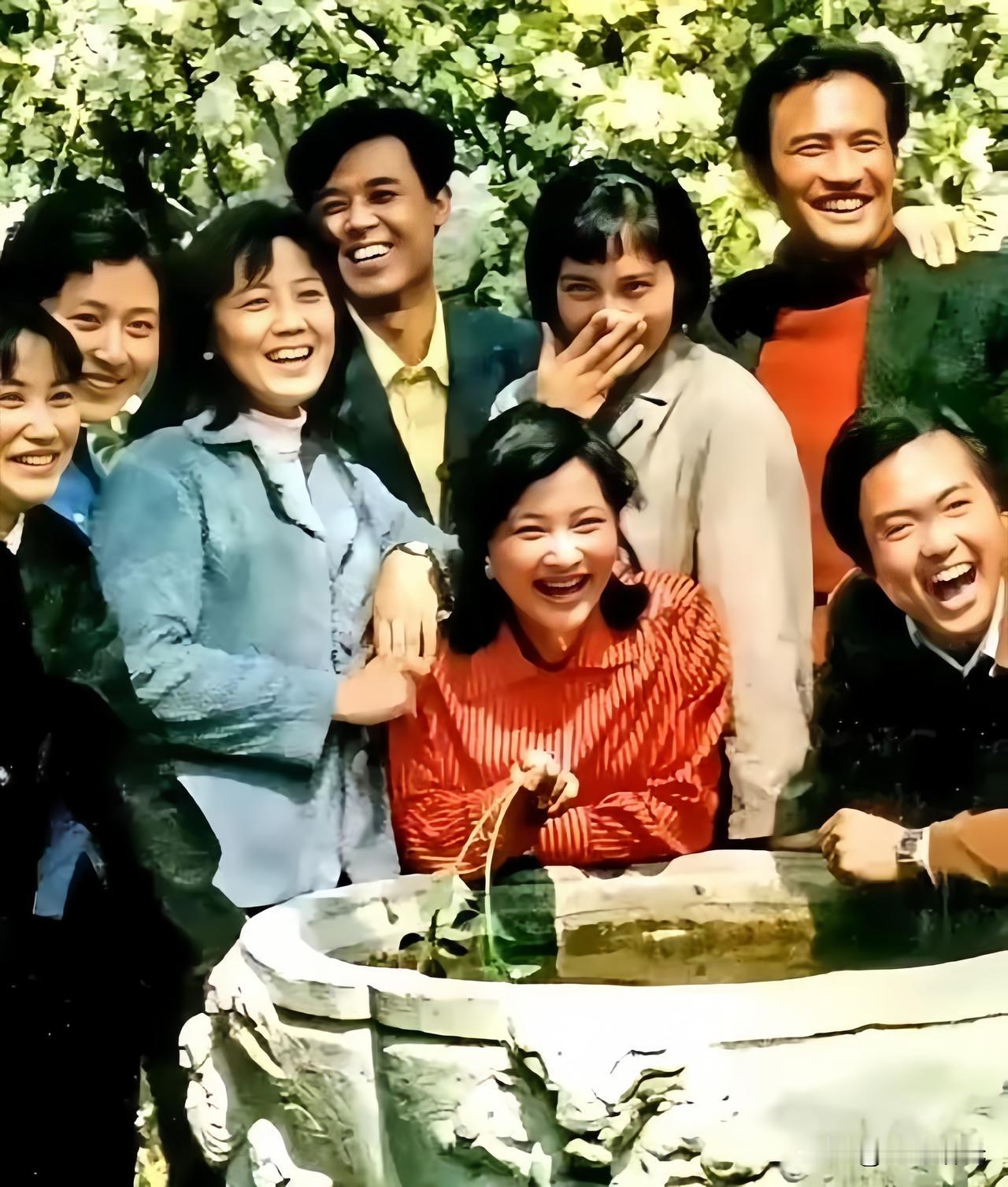 🎬 这张照片拍摄于1980年。
在开满花树的庭院里，演员们围在大水缸旁，没有摆