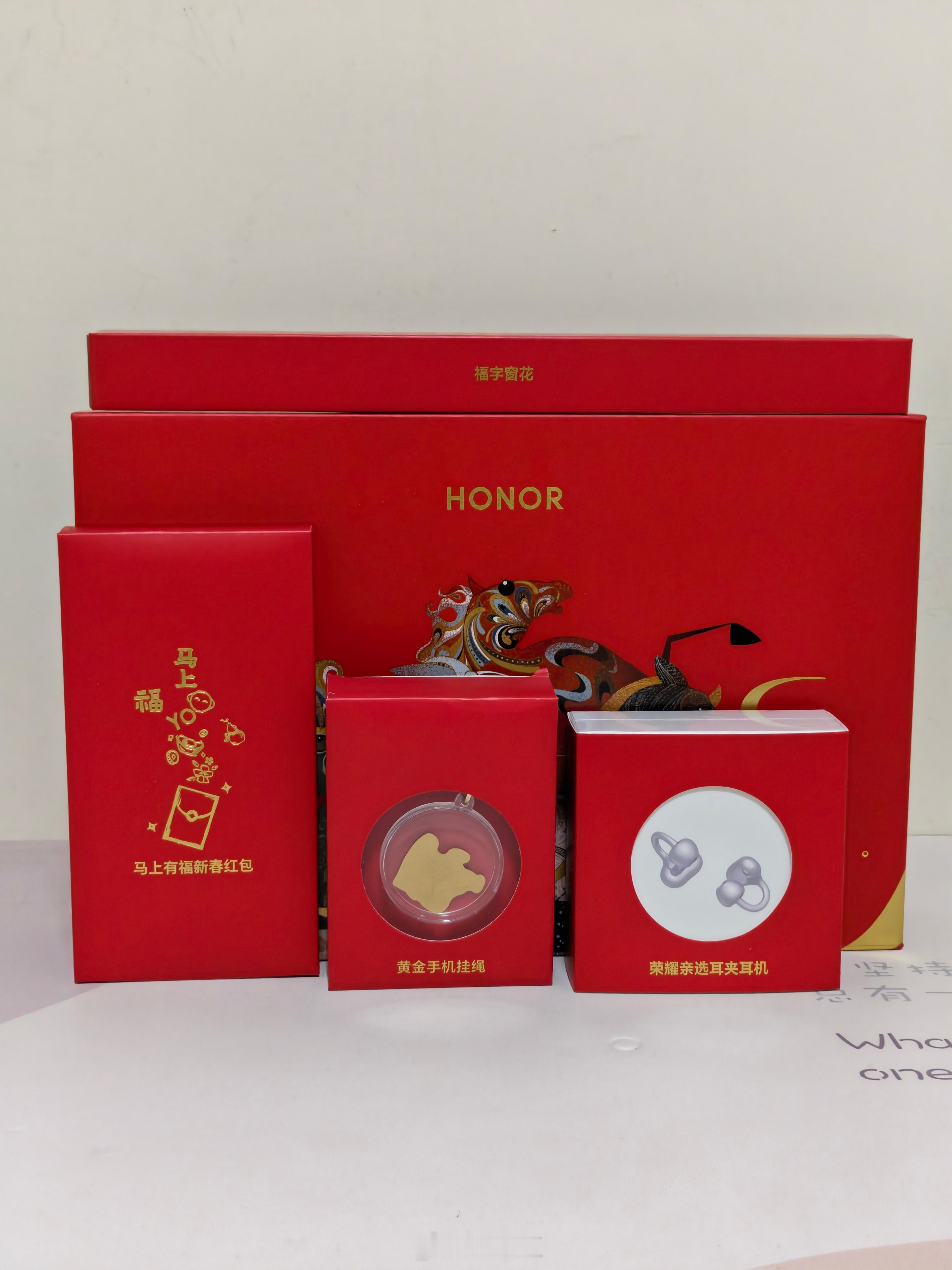 收到了荣耀新年礼盒，里面有荣耀亲选耳夹式耳机、“马上YO钱”足金手机挂饰、新年窗