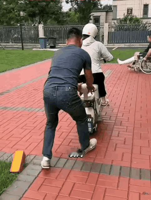 丈夫教妻子骑电动车，刚把手撒开，妻子摇摇晃晃的往前骑。一名腿上缠着绷带的男子坐轮