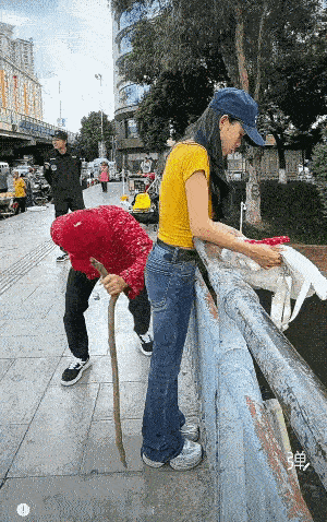 老者身穿红色花衣，头戴红色帽子，拄着拐杖在桥上行走，一不小心撞到了时尚的小姐姐，