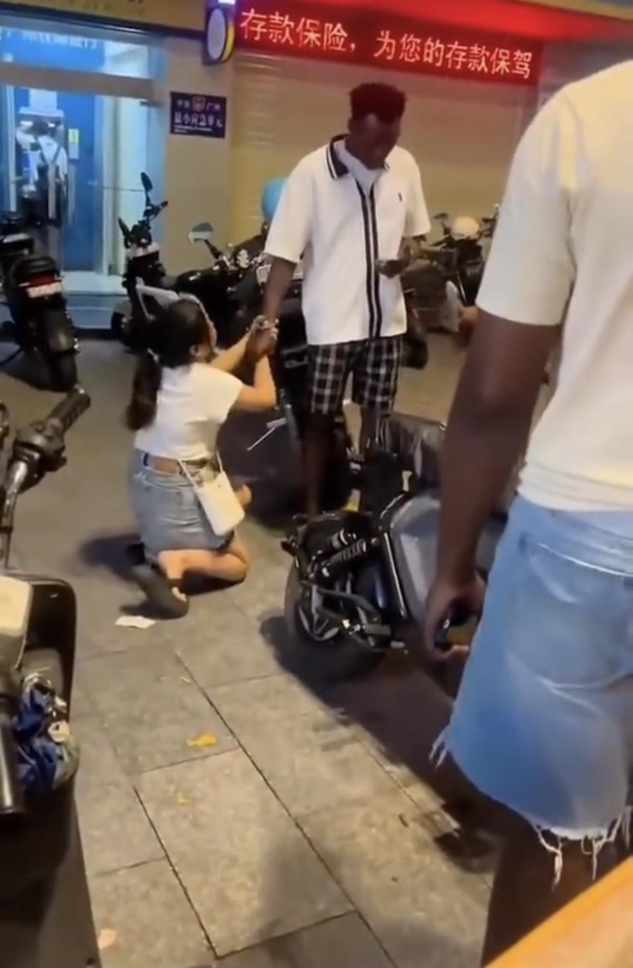 一名在广州的中国女子跪在其黑人男朋友脚下，双手抓着黑人的手，不愿放手，不想让这位
