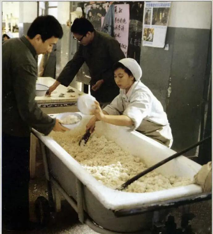 80年代的清华，食堂用大浴缸装米饭，学生们常在校道旁蹲着用餐。 