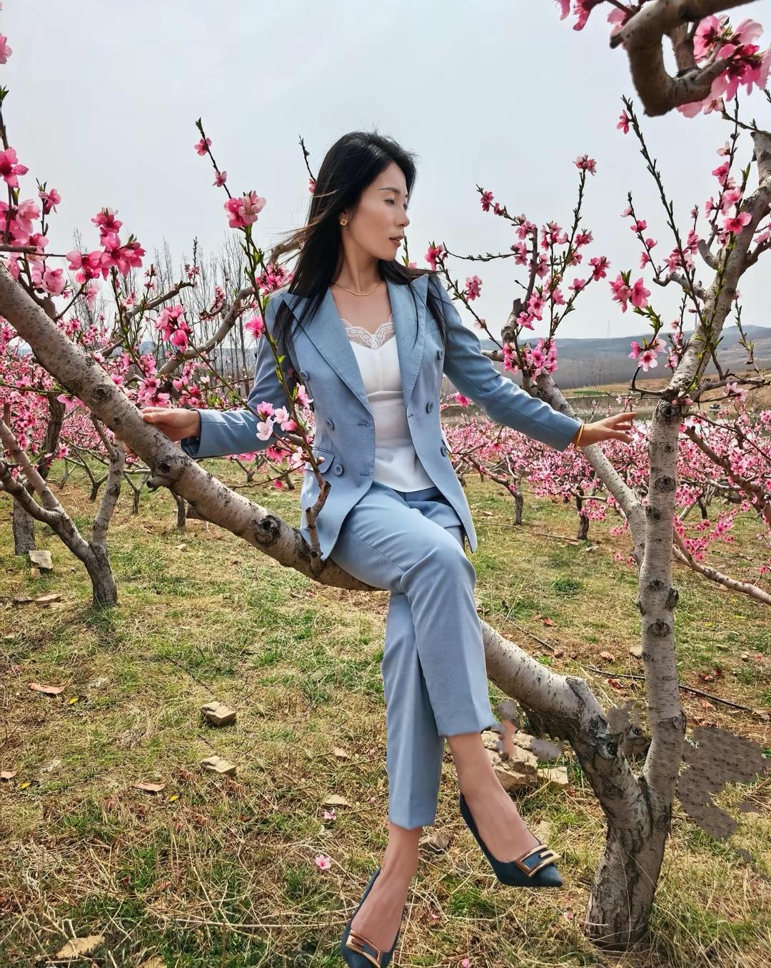 穿西装的美女坐在开满花的树上。