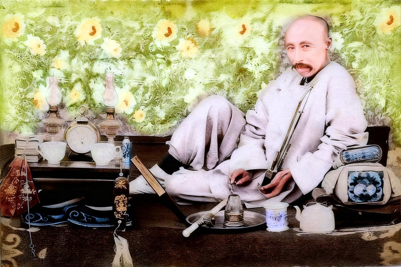 清末时期，一名男子斜靠在卧榻的枕头上，眼神颇为邪魅地看着镜头。他手里抱着水烟斗，