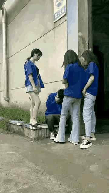 工厂车间的外侧，男员工被三个年轻的女员工围住说笑，他用手捂住脸部，表现的羞涩胆怯