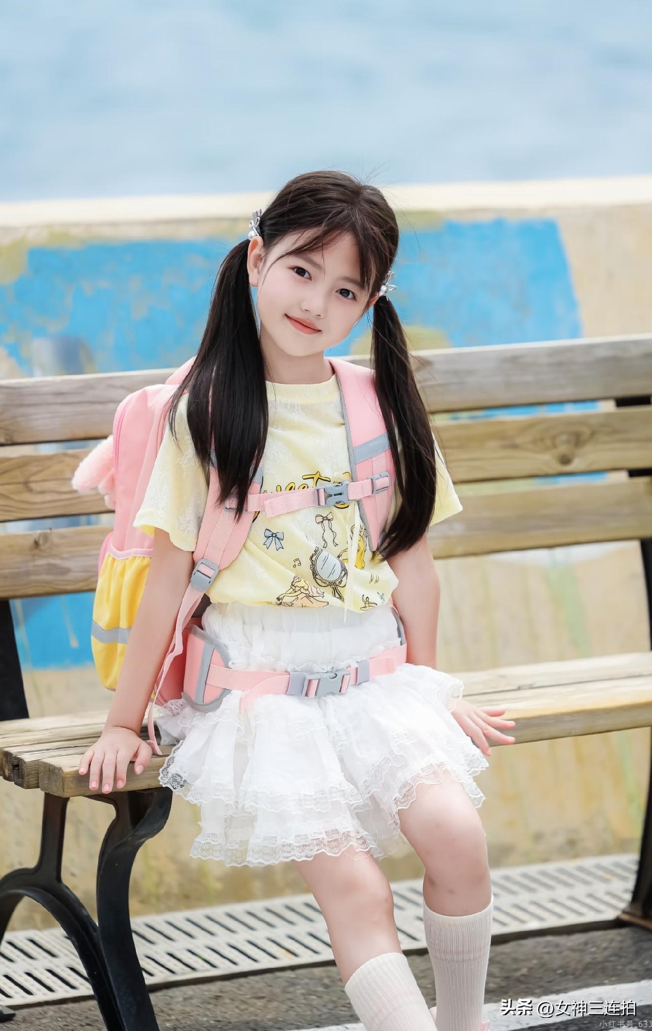 小妹妹背着书包坐在长椅上。