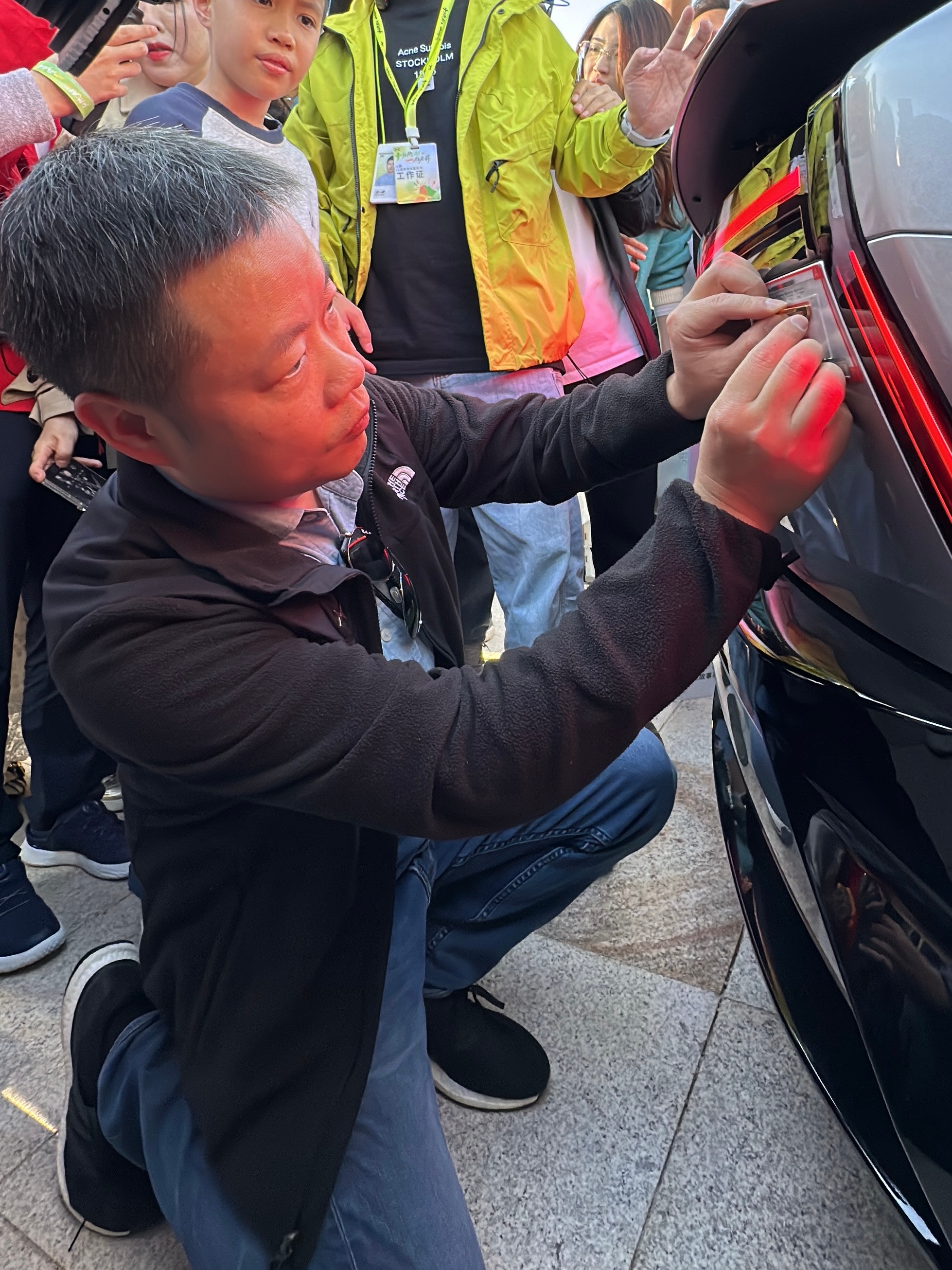 何小鹏蹲下帮车主贴24K金车标，实名羡慕小鹏P7初代车主了，而且金标含金量从18