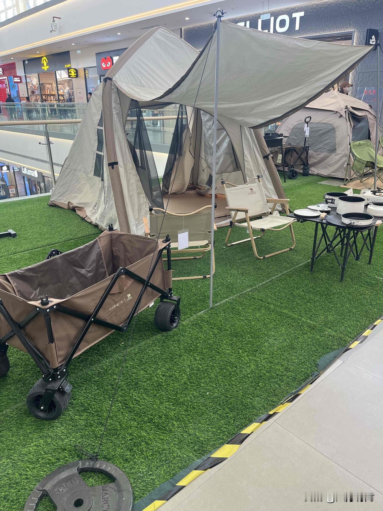 商场里支起的露营角太戳心啦！

卡其色帐篷配遮阳天幕，折叠椅、小推车、露营锅具摆