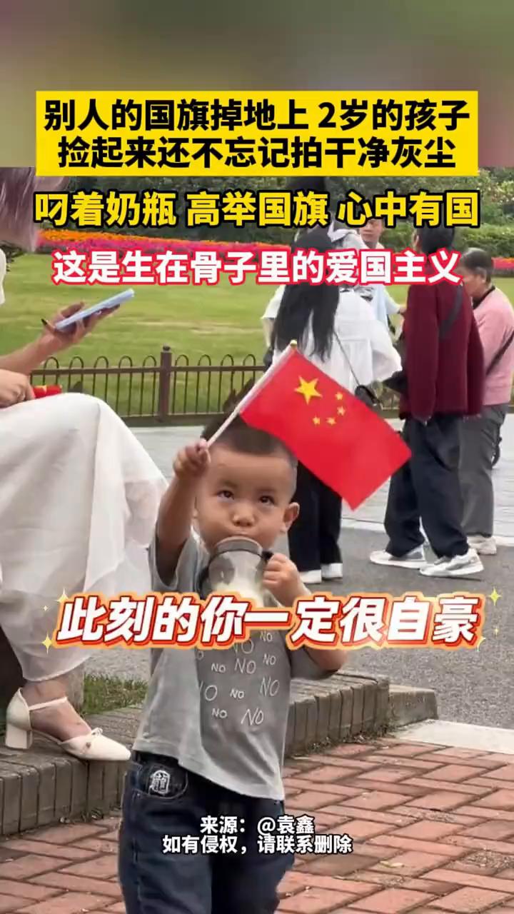别人的国旗掉地上，2岁的孩子捡起来还不忘记拍干净灰尘，叼着奶瓶高举国旗心中有国，