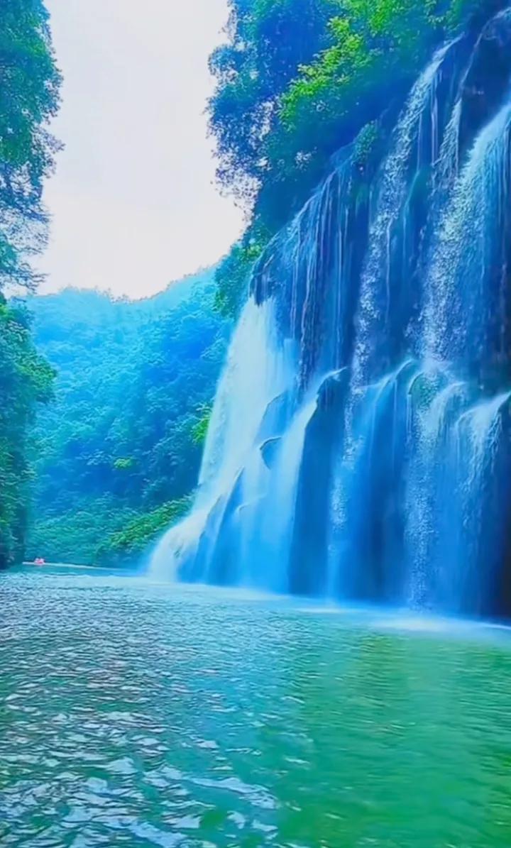 瀑布飞流直下，如银河落九天，碧水清澈见底，绿意盎然。群山环绕，云雾缭绕，宛如仙境