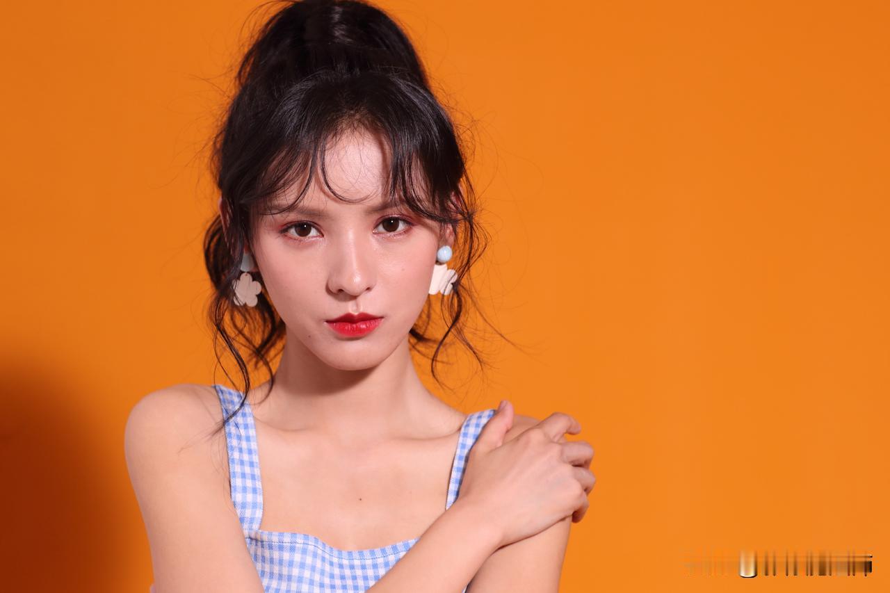 当明橙色背景撞上蓝白格吊带裙，张予曦将夏日调成了一杯气泡感的橘子汽水。高马尾垂落