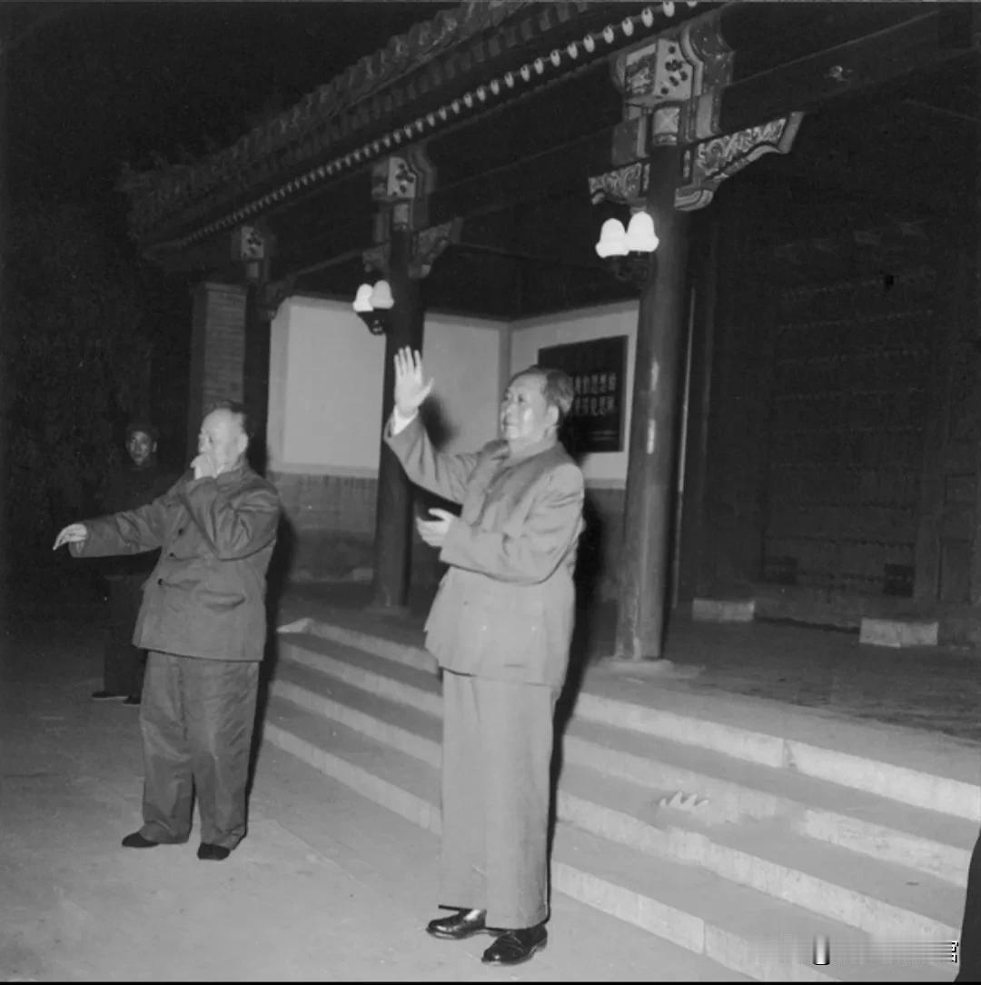 这张黑白老照片拍摄于夜晚的中南海，毛主席身着中山装，站在古建筑台阶前挥手致意，身