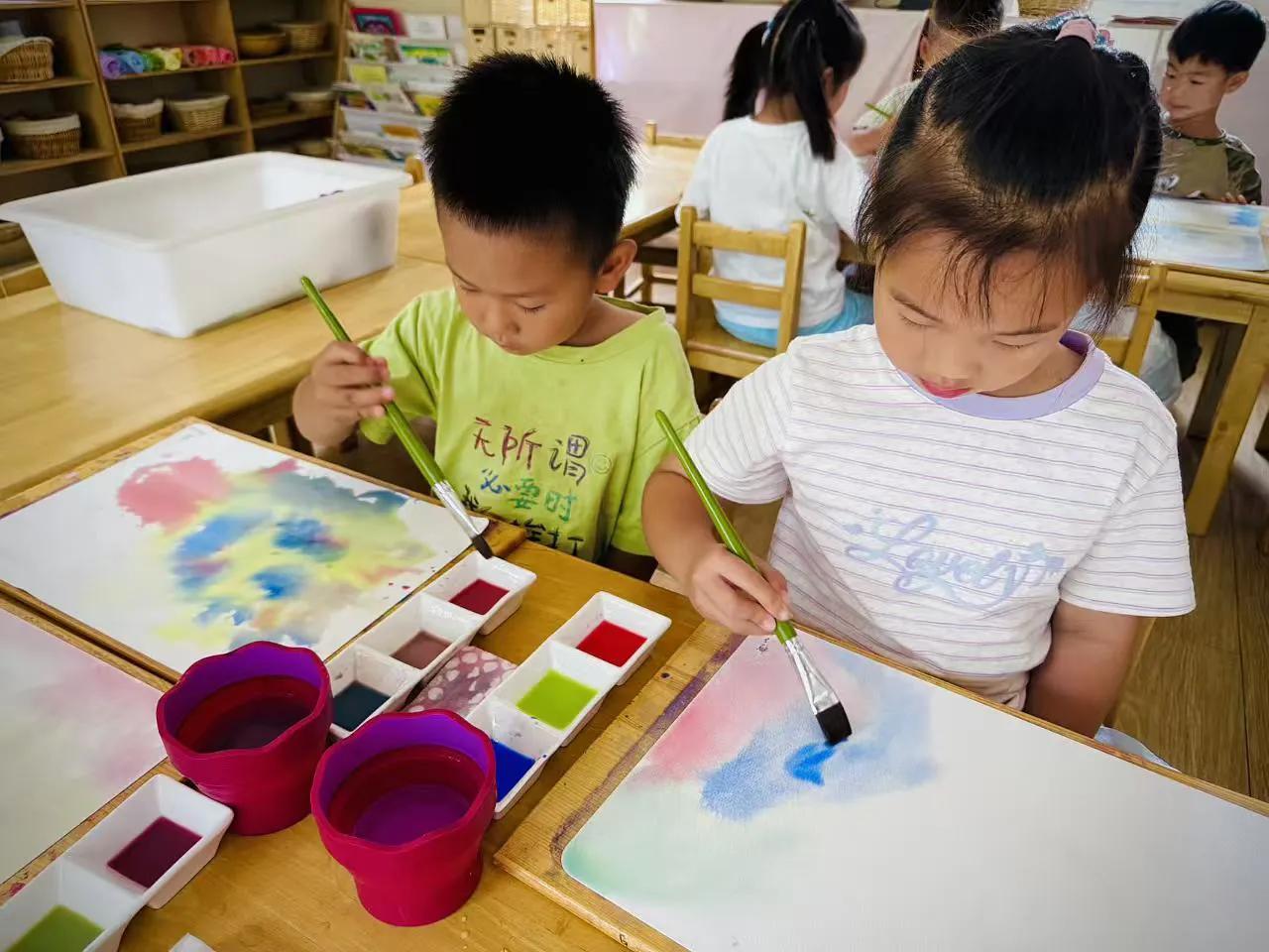 美术课上，幼儿园的小朋友们捧着水彩盘认真作画。笔尖蘸上清水，各色颜料在画纸上晕开