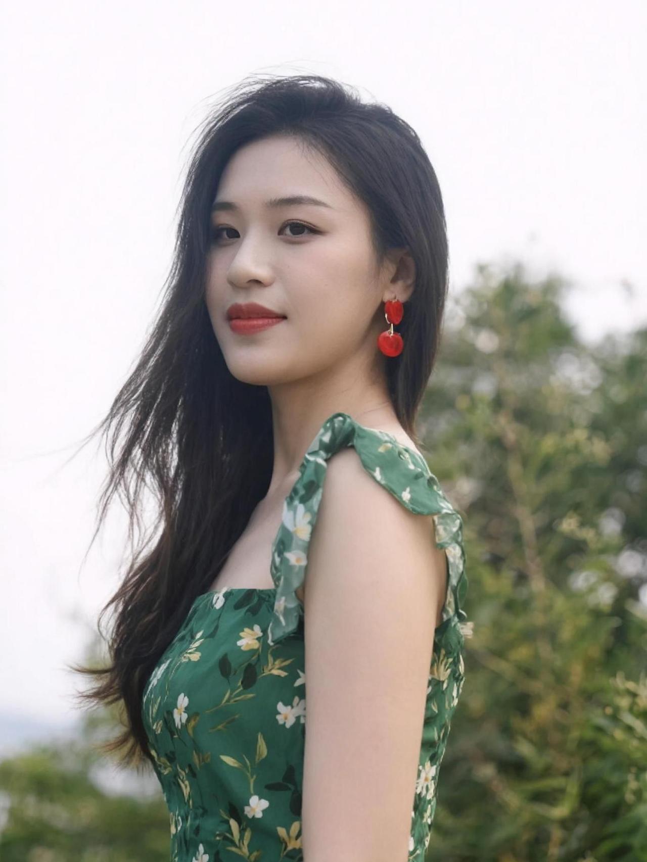 在绿意盎然的背景中，碎花裙与阳光交织成一幅温柔的画卷。耳畔的红色耳饰如同点睛之笔
