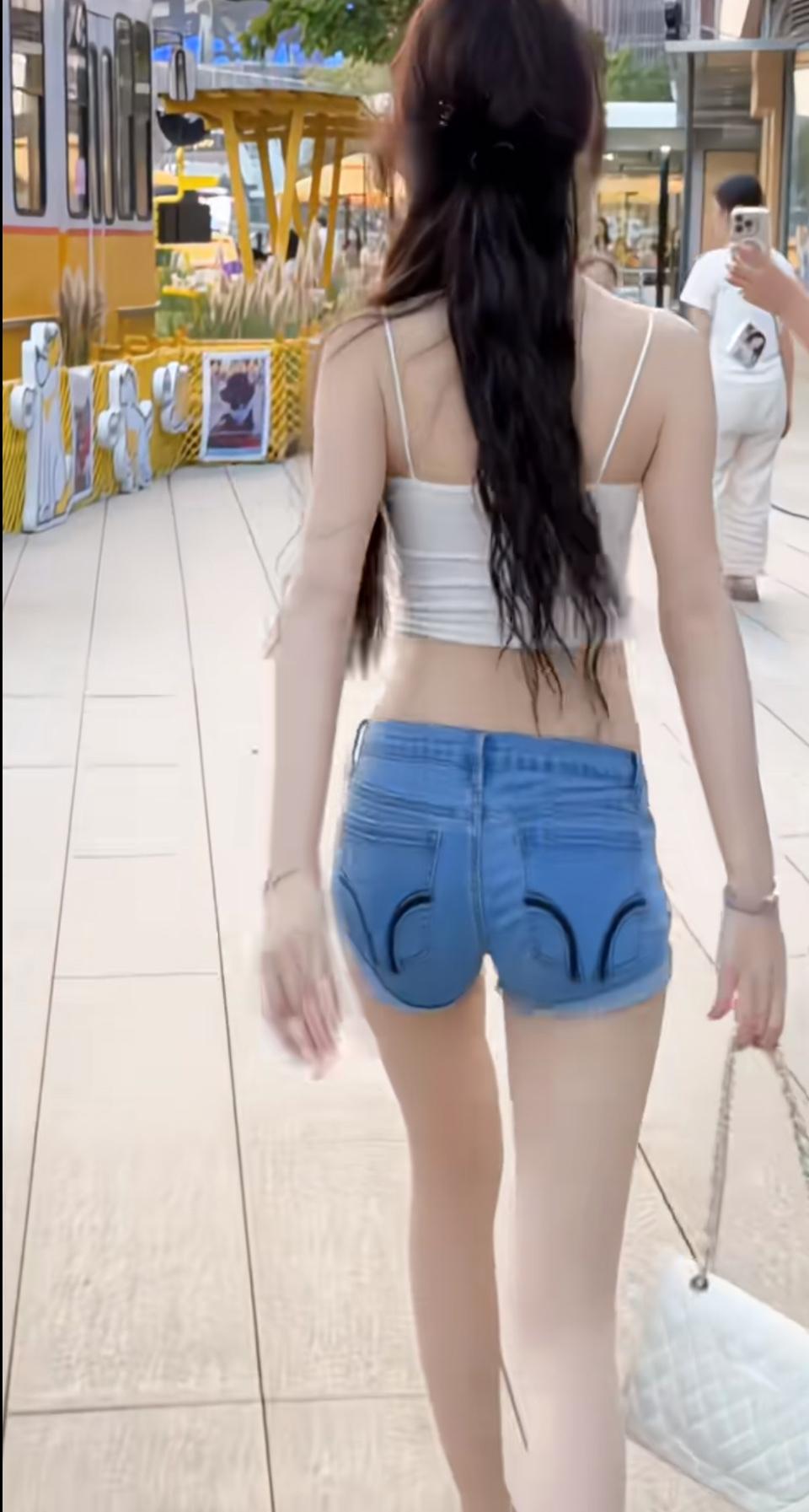 吊带露腰搭牛仔热裤，长发扫过腰线的弧度刚好。提着白包走在街景里，每一步都漫着松弛