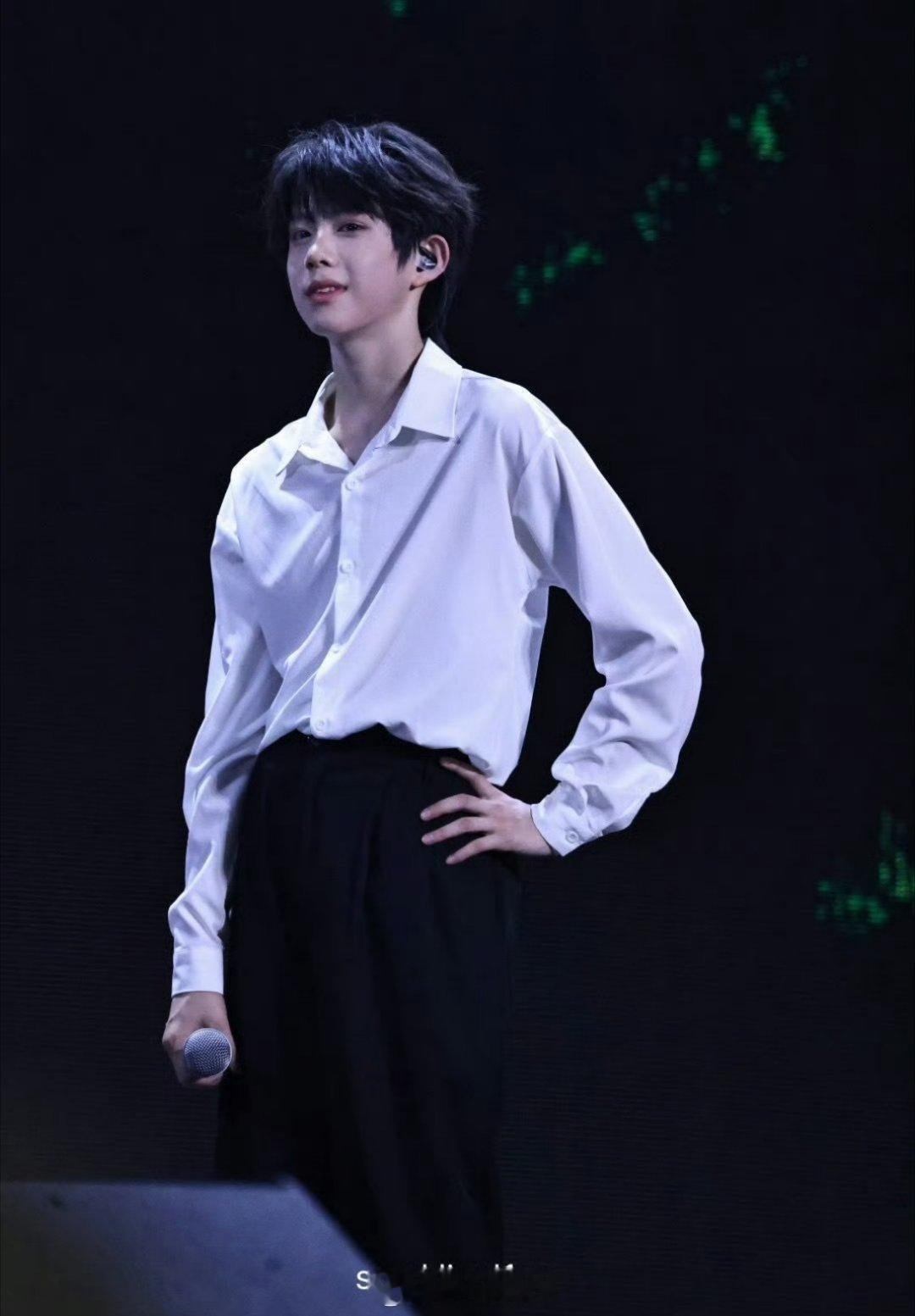 陈奕恒的公演舞台饭拍图，白衬衫配黑色长裤，站在舞台上还蛮放松的，这小伙子简直不要