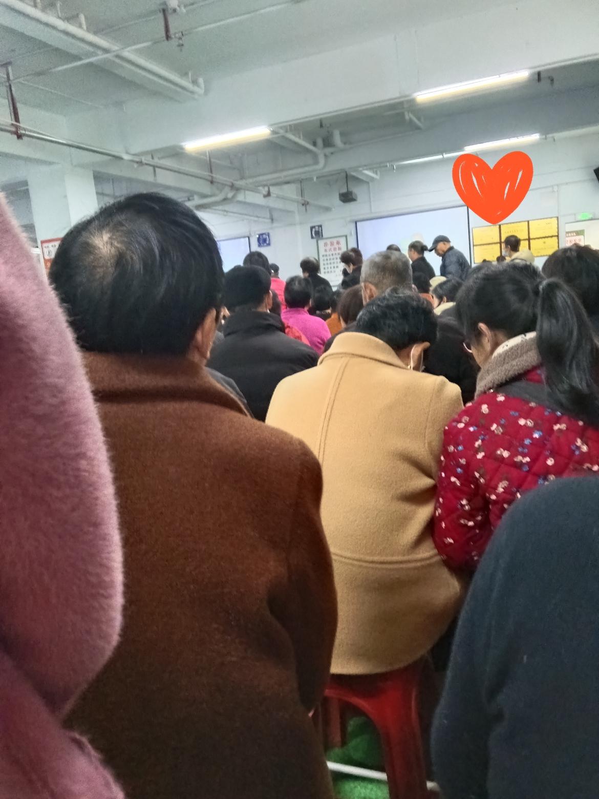 这张图里是个室内场地，好多人坐小马扎挤一块儿，看背影大多是中老年人，穿得都挺厚实