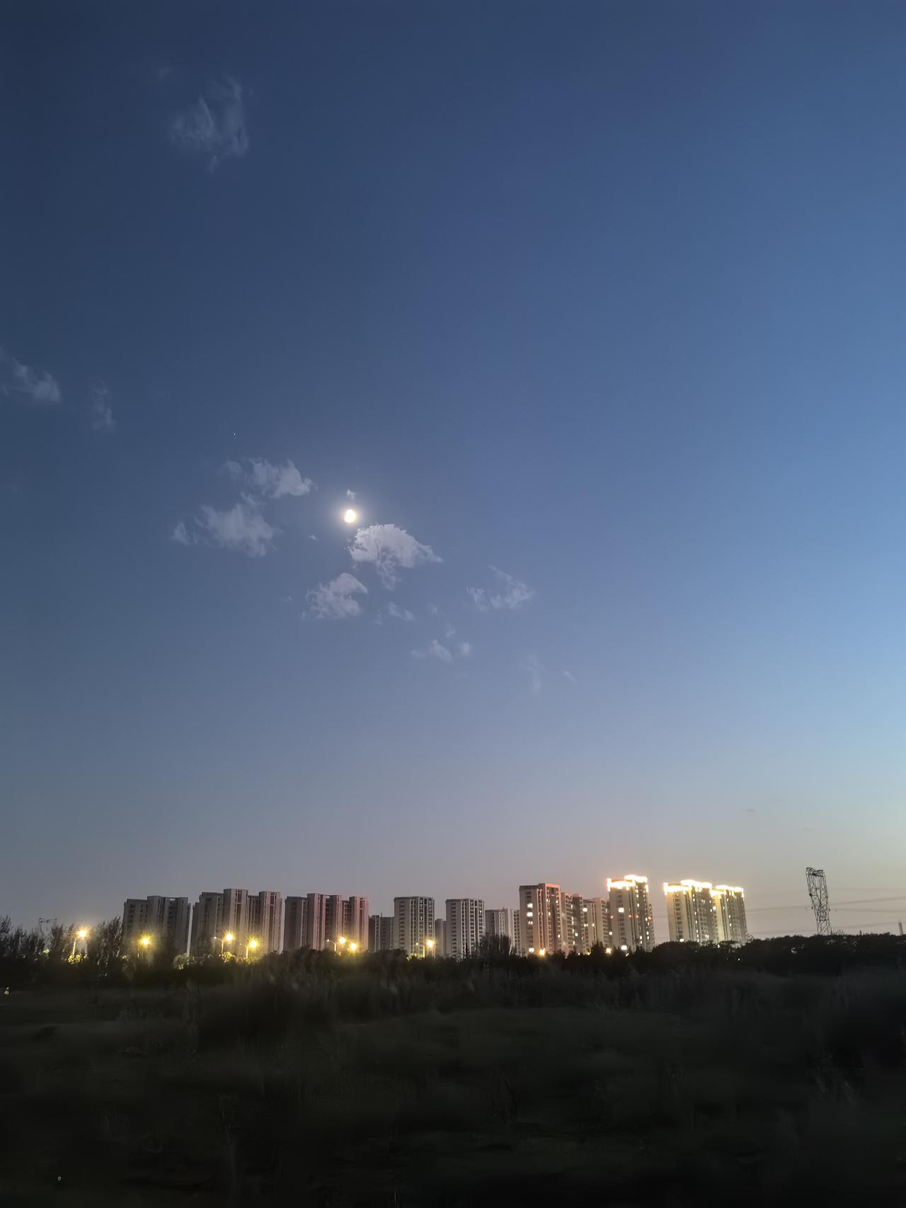 黄昏时分，城市灯火初上，天边明月高挂。