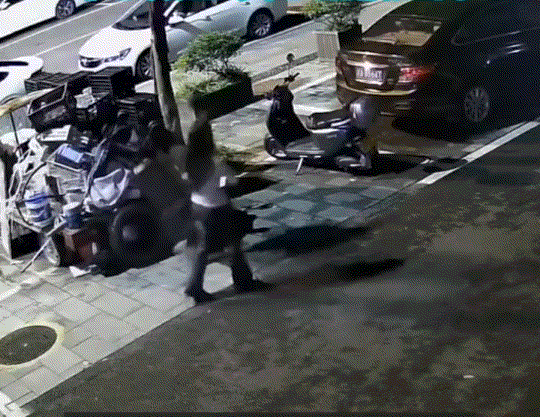 重庆，一对情侣同行走在街头时，这男子不知何故，上前就将路边停放的电动车猛地踢倒后
