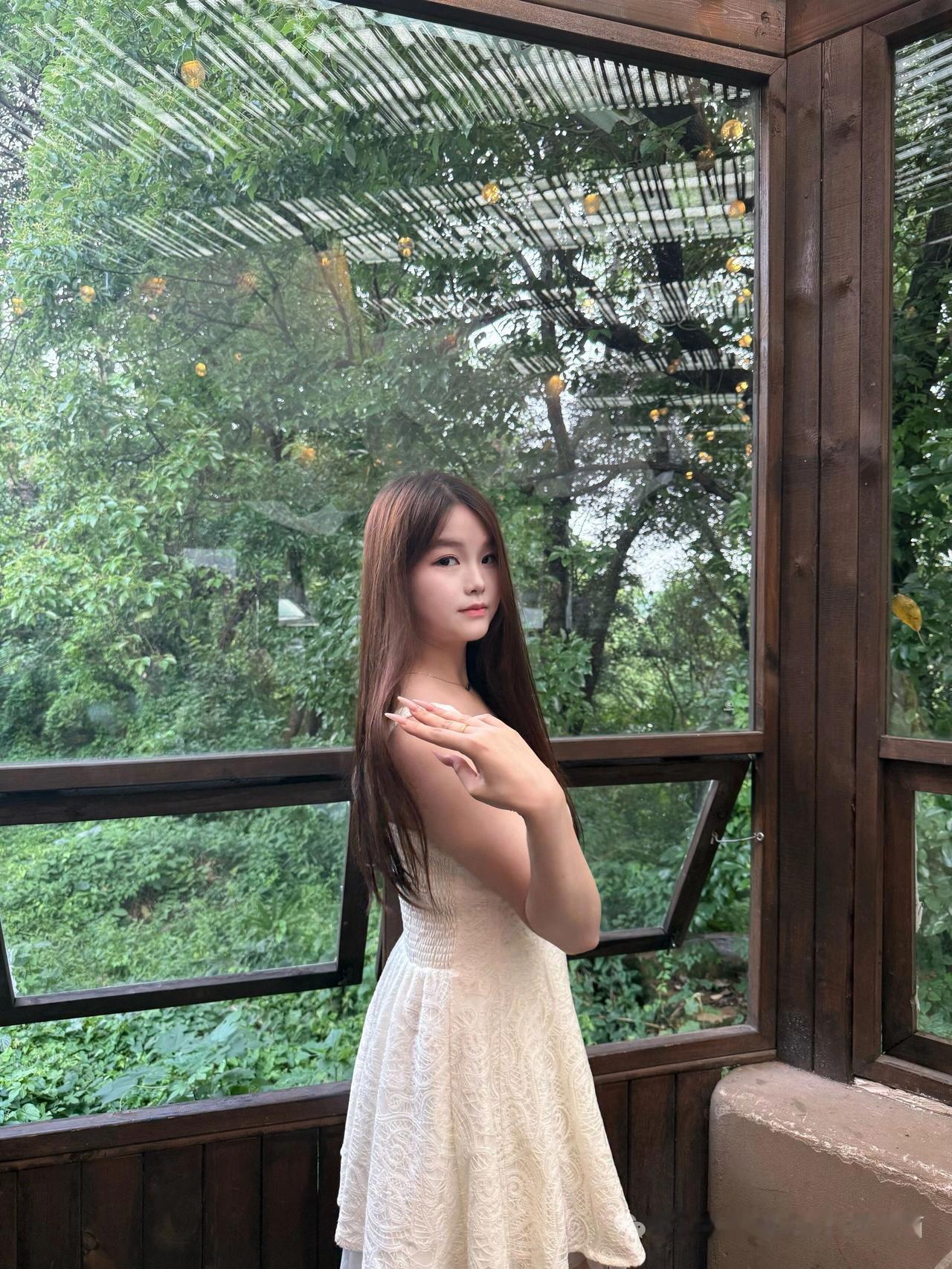 一个女孩站在木窗边，手托着下巴。