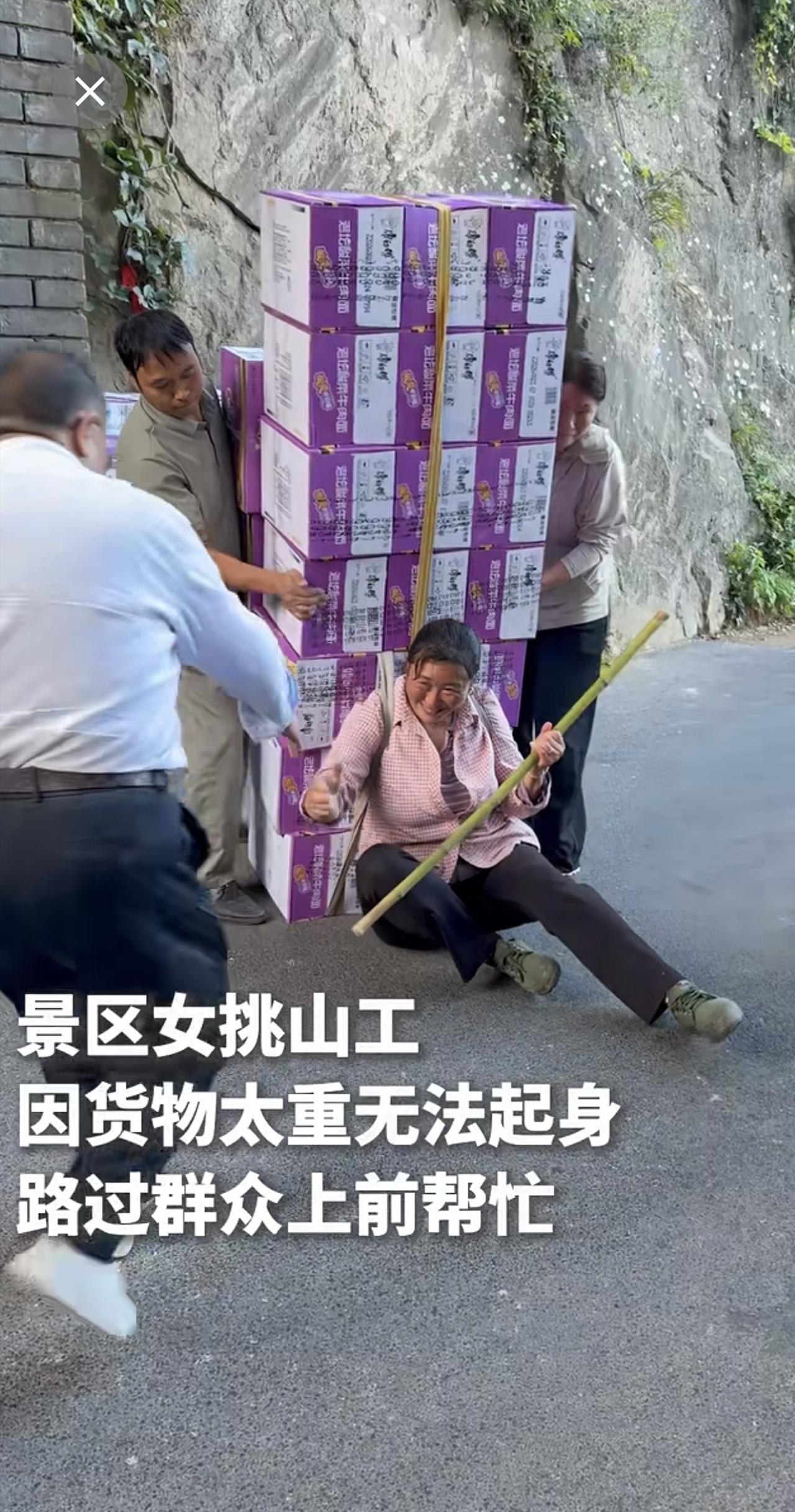 景区女挑山工因货物太重无法起身，路过群众纷纷上前帮忙。（素材来源：网友“暴走灰太