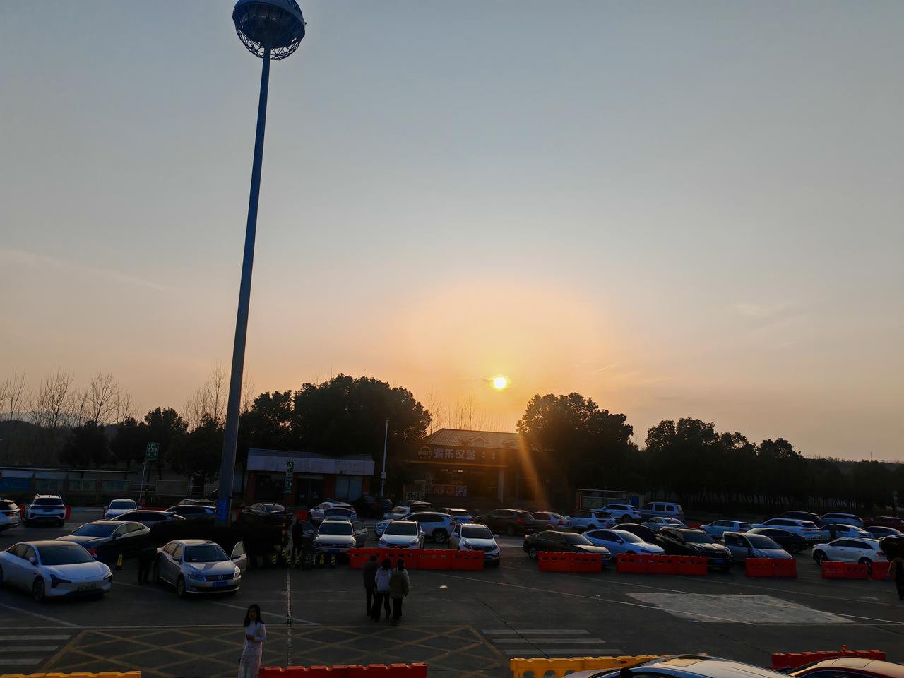 分享一张在路上的风景落日为服务区镀上一层柔和暖光，夕阳悬在天际，晕染出淡淡的橙黄