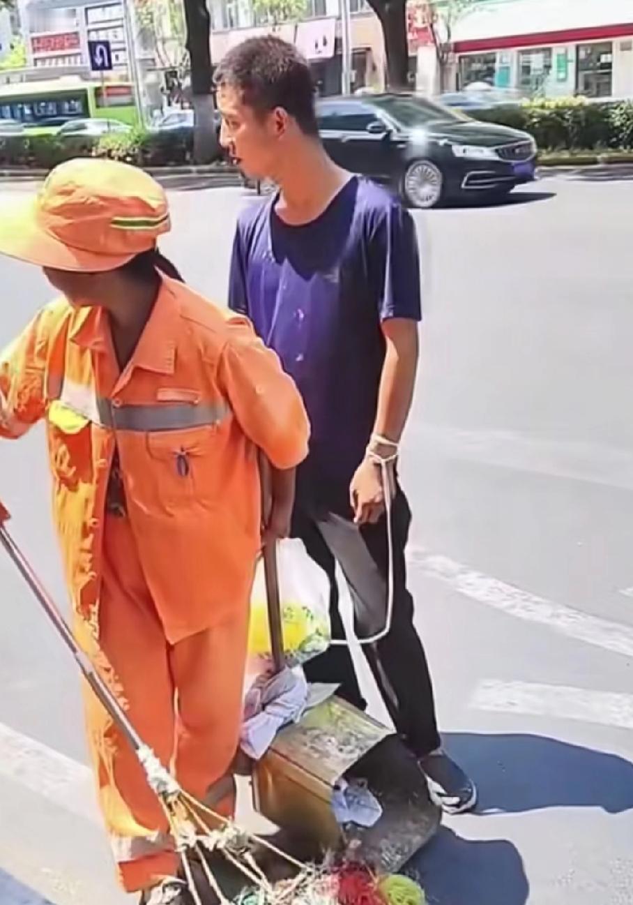 大太阳的，一位环卫大姐顶着大太阳在清扫马路，旁边一男孩，紧紧跟着，原来是大姐的智