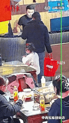 一个穿着旧棉袄的女人，怀里抱着一个三四岁的男孩，站在一家早餐店门口，久久没有进去