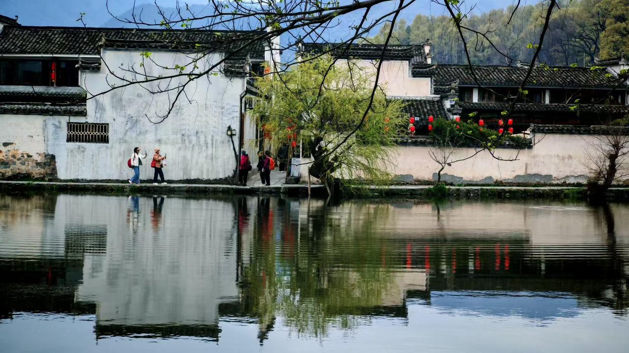 春水漾开徽州韵，白墙黛瓦映清波。枝头新绿初绽，行人漫步画中，这般水乡景致，最是能