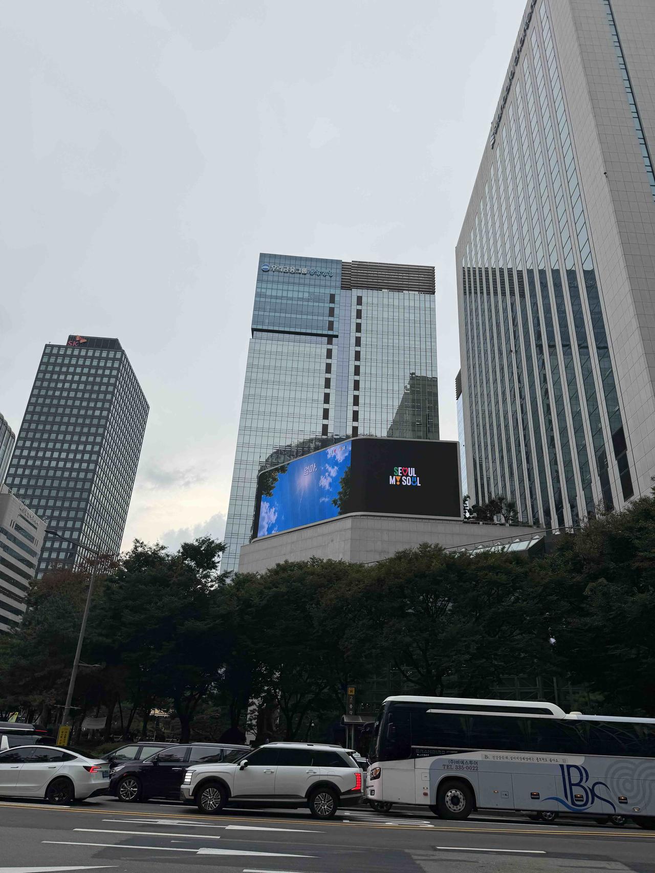 首尔街头高楼林立，大屏写着“Seoul My Soul”，车流穿梭间，城市也在悄