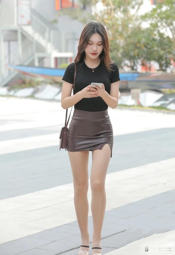 一个女孩在街上看着手机。穿褐色群的时尚女生