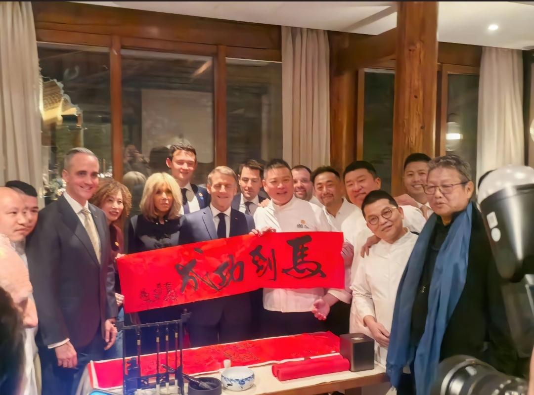 马克龙和布里吉特在酒店内，与厨师们热情互动，在吃饭前，有一个写毛笔字环节，送给夫