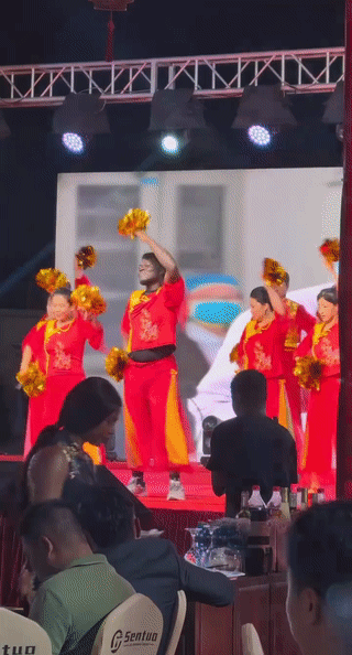 一名黑人男子站在舞台上领着大爷大妈跳舞。
看起来跳的非常卖力，真是深受大家的喜爱