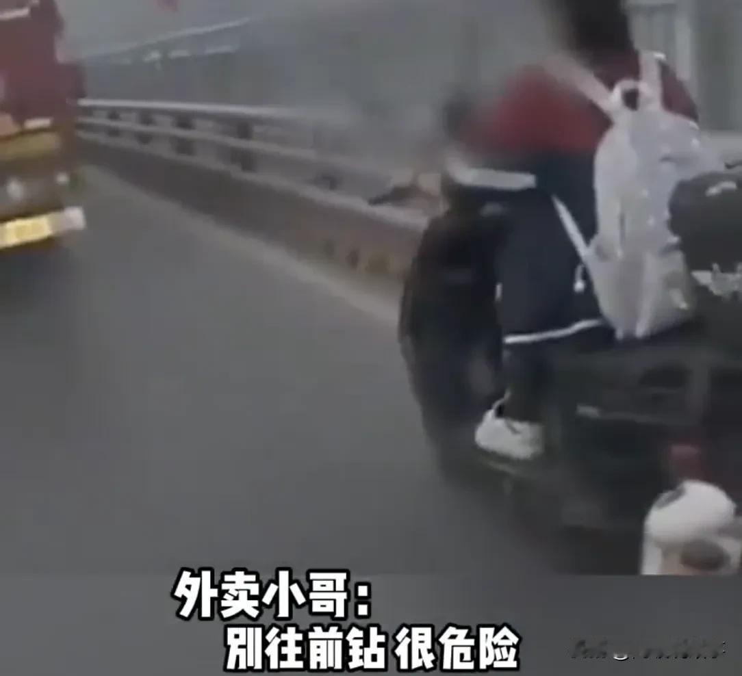 外卖小哥见女孩贴着大货车超车，忙喊："别钻，危险！"谁知，女孩回头瞟了一眼后，继