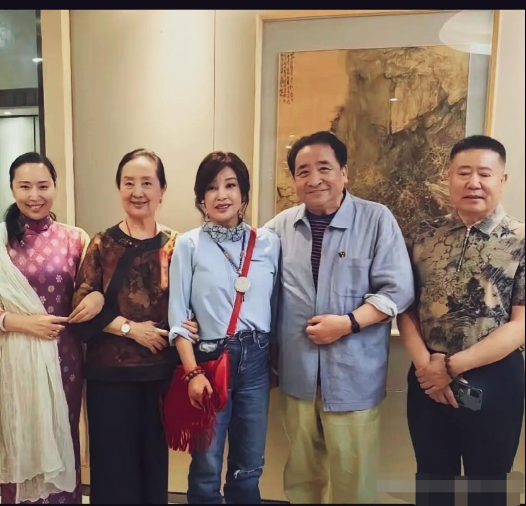 中间是刘晓庆，一身浅蓝上衣搭配牛仔裤，挎红色流苏包，打扮的像四五十岁，身旁站着姜