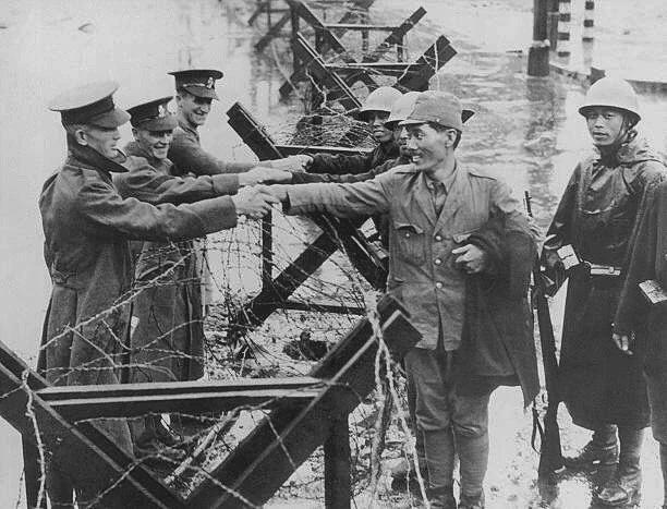 1937年的黑白照片：在上海公共租界内，几名英军士兵隔着铁丝网路障，正与日军士兵