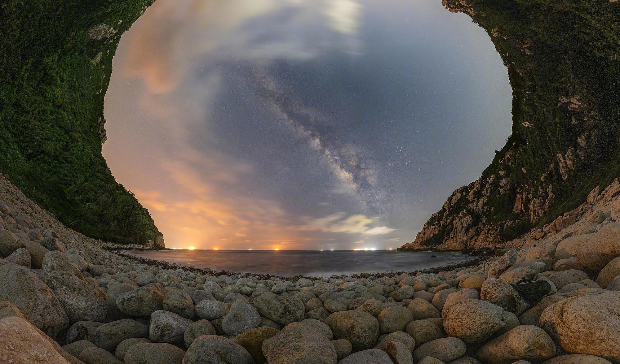 圆石如棋子，密密匝匝铺满海湾，一直延伸到潮水边缘。夜空被两侧的山崖框成一扇穹窗：