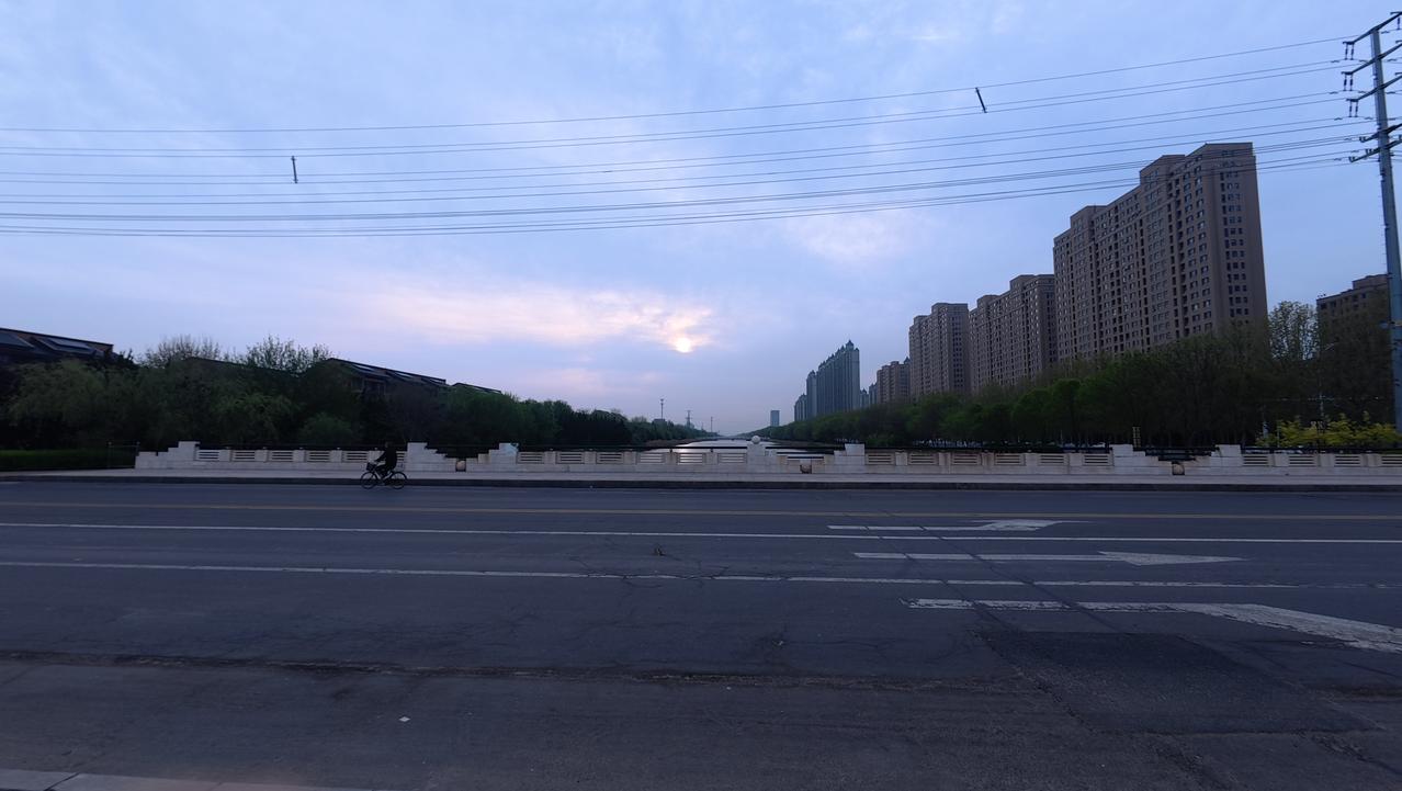 春日生活打卡季暮色四合，河畔尽显城市温润。澄澈水面倒映着林立高楼，岸边绿树与建筑