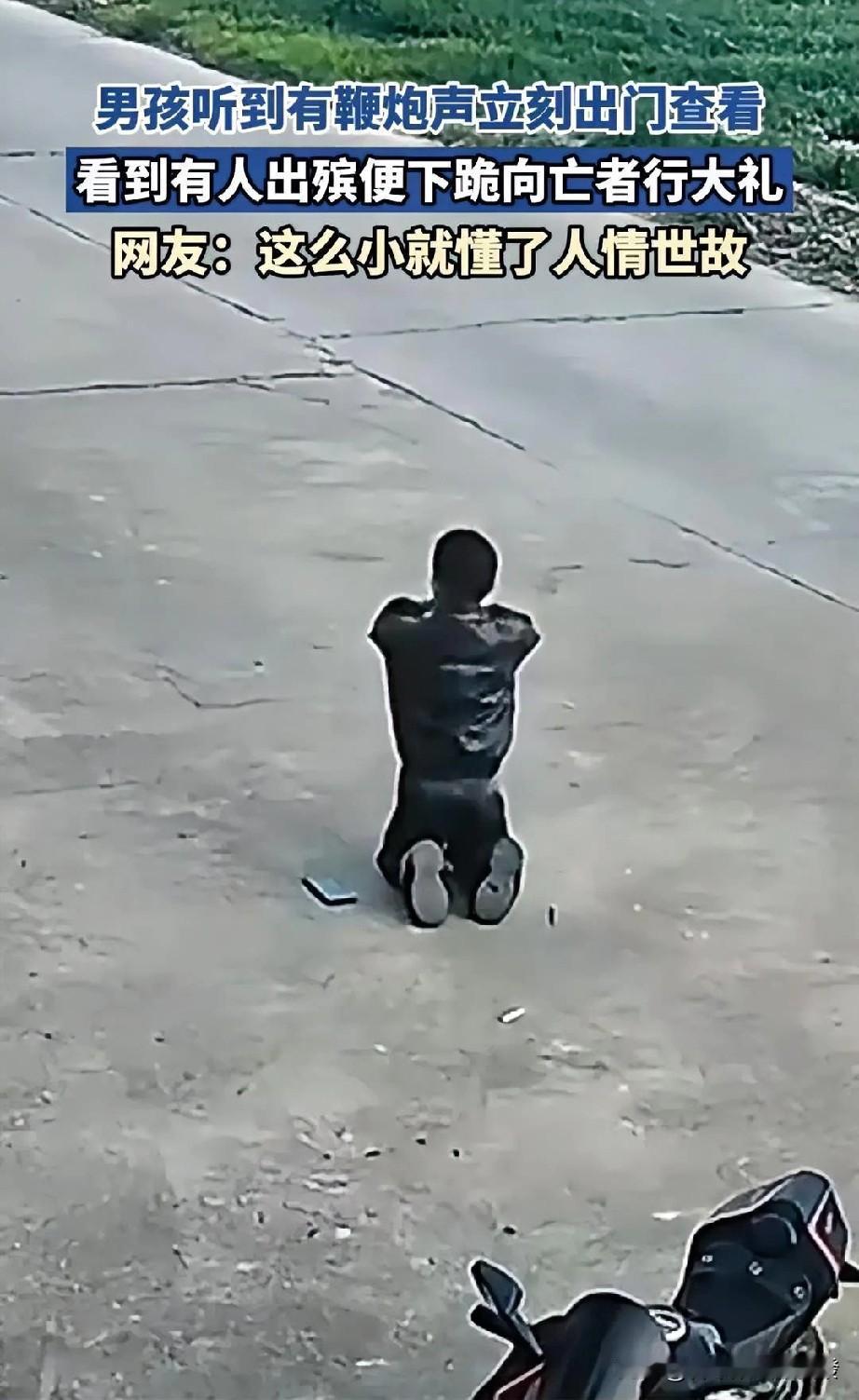 一阵鞭炮声响起，小男孩听到后赶紧从屋里跑了出来，当看到是有人出殡时，立马把拿着的