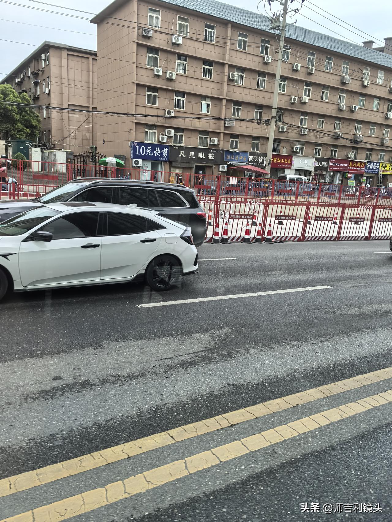立交桥北侧坡头，玉泉东路红绿灯十字路口，人行道上也有好多红色的围挡，穿绿色工服的