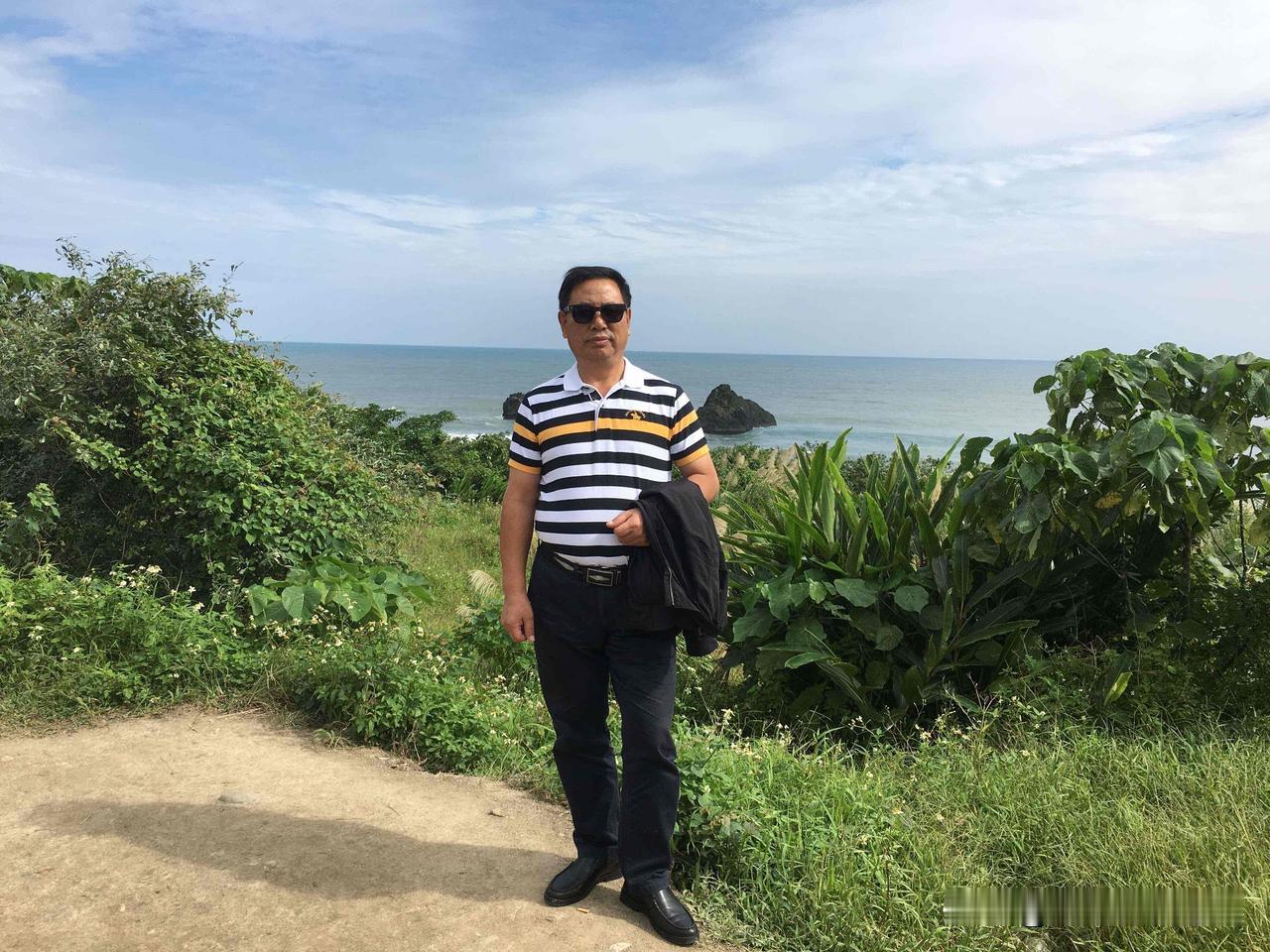 你手机里哪张夏日照片最美身着条纹Polo衫、佩戴墨镜，站在临海观景步道上，两侧草