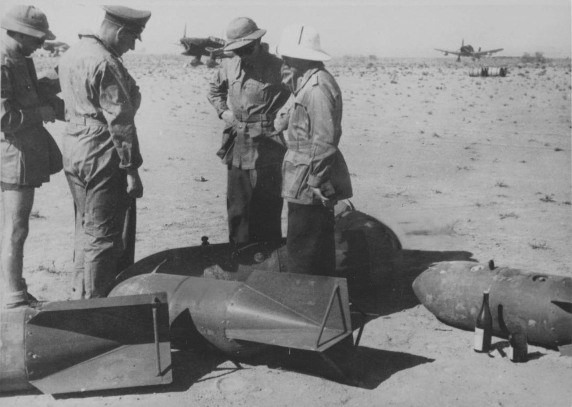 1941年，北非，在某野战机场上，德国空军军官正在检查航空炸弹，远处背景是容克 