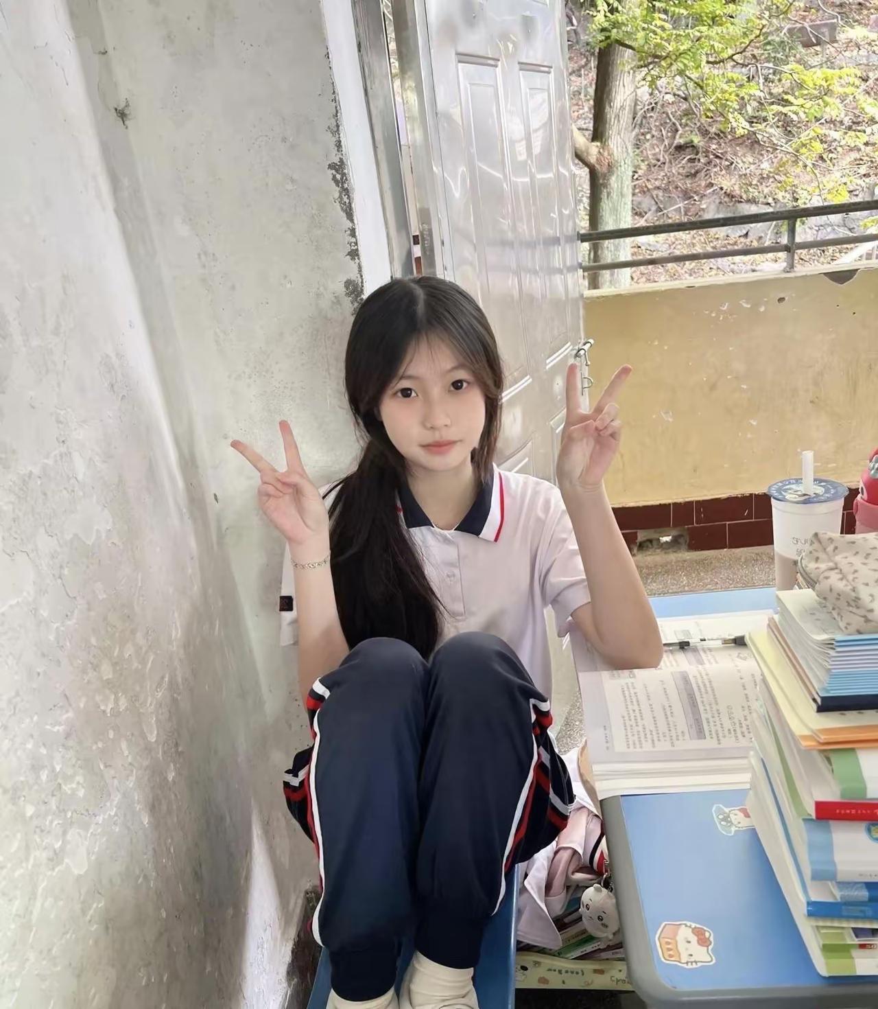 她坐在墙边，双手比着“V”字手势。甜系手势写真 脸颊比心 比心