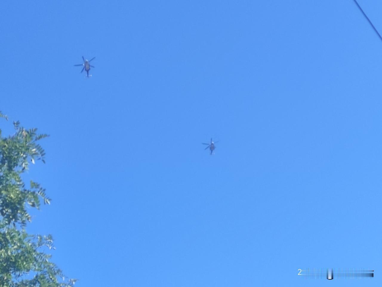 空中共有两架军用运输直升机编队飞行，从仰视角度能清晰看到主旋翼与尾桨轮廓，机身呈