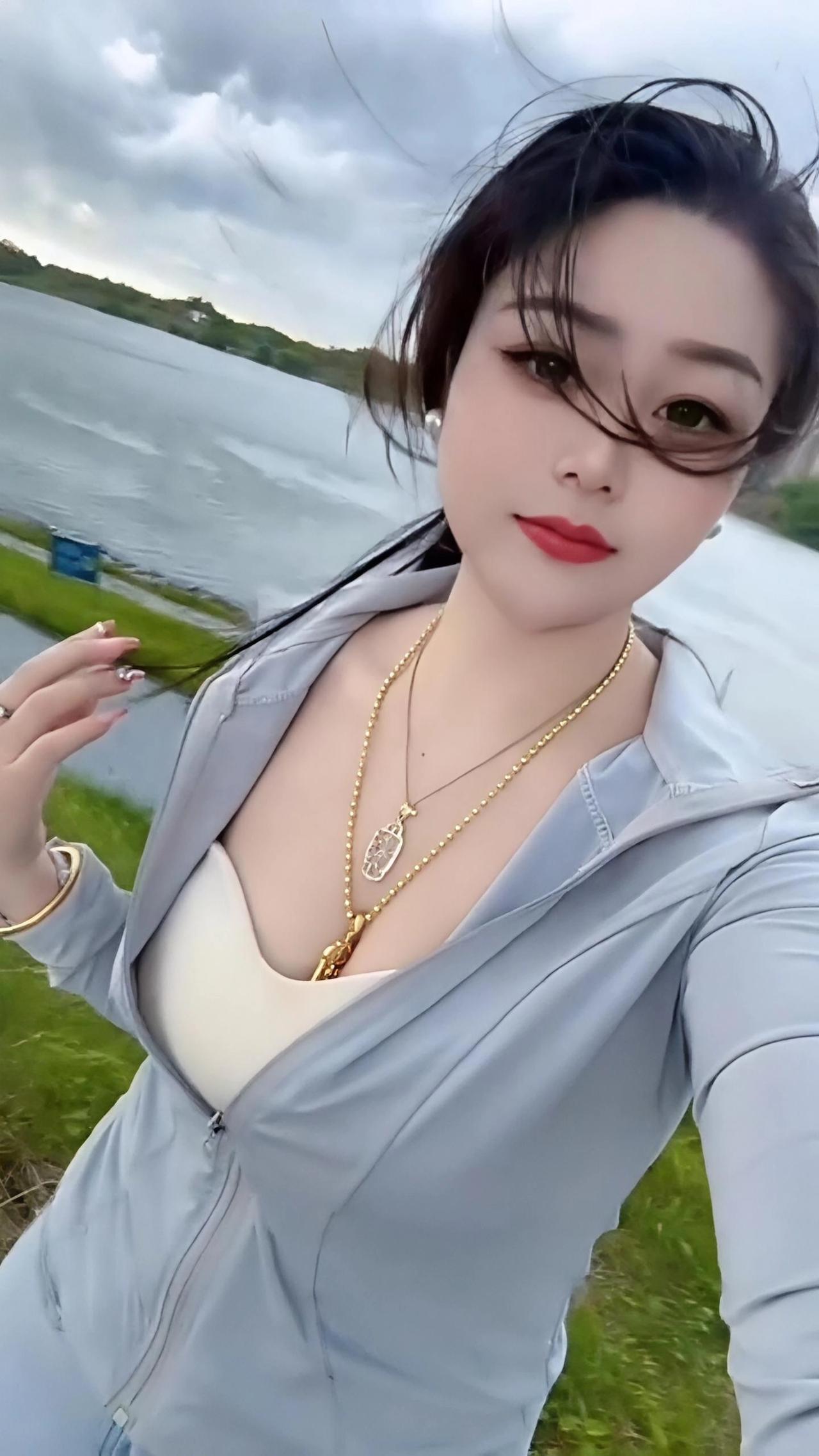 真是太美了，湖畔微风轻拂，发丝随性飞扬，浅灰防晒衣衬得气质清爽温柔，叠戴的金饰精