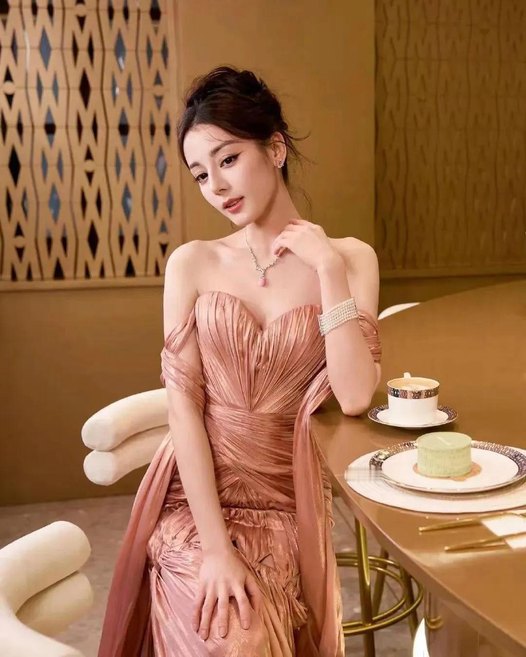 迪丽热巴以一袭粉色抹胸开叉长裙，缓缓步入这梦幻般的摄影空间，仿佛是从春日里最温柔