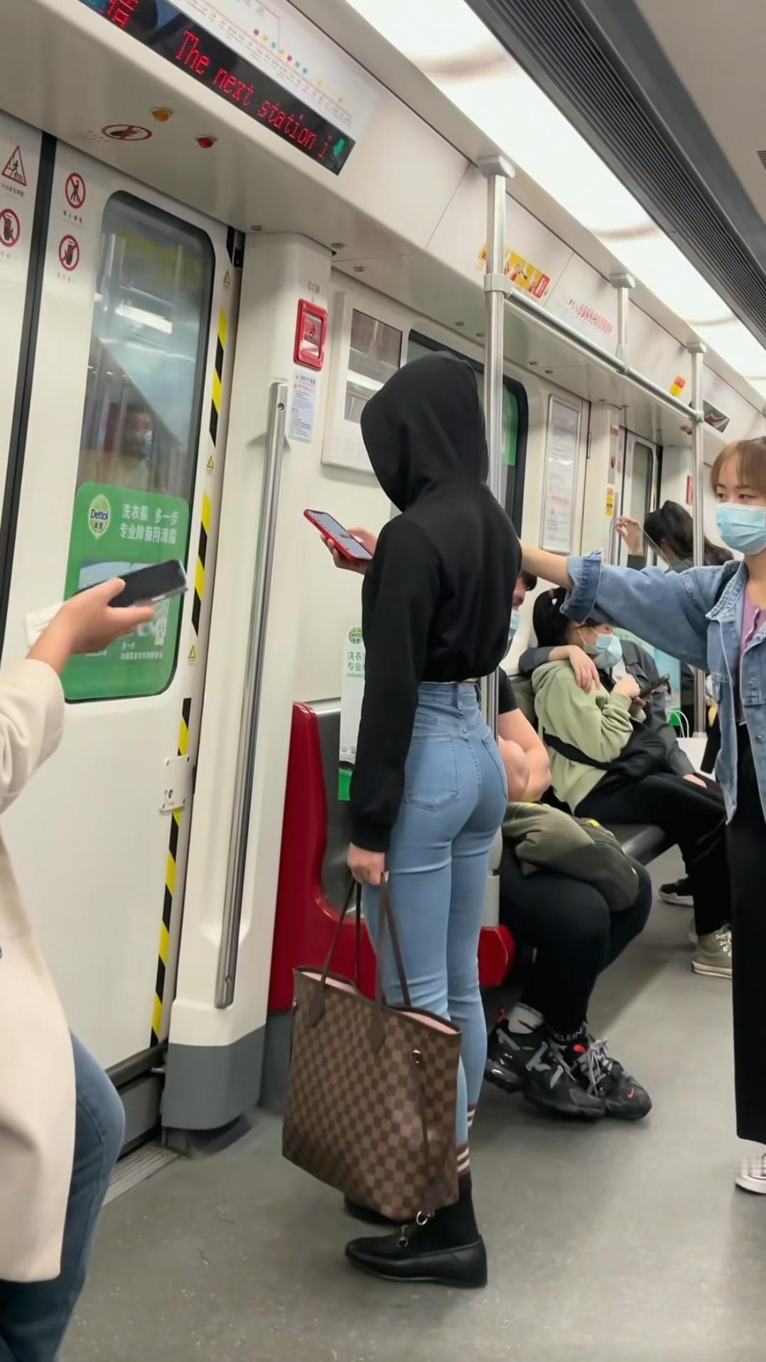 地铁上的时尚穿搭，黑色连帽衫搭配蓝色牛仔裤，手提包显时尚
