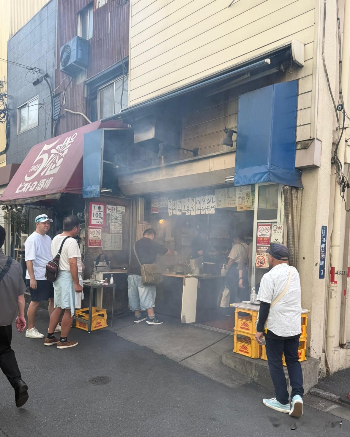 东京路边烤串店。一个鸡肉串100日元。
客人站着一边吃着鸡肉串，
一边喝着啤酒?