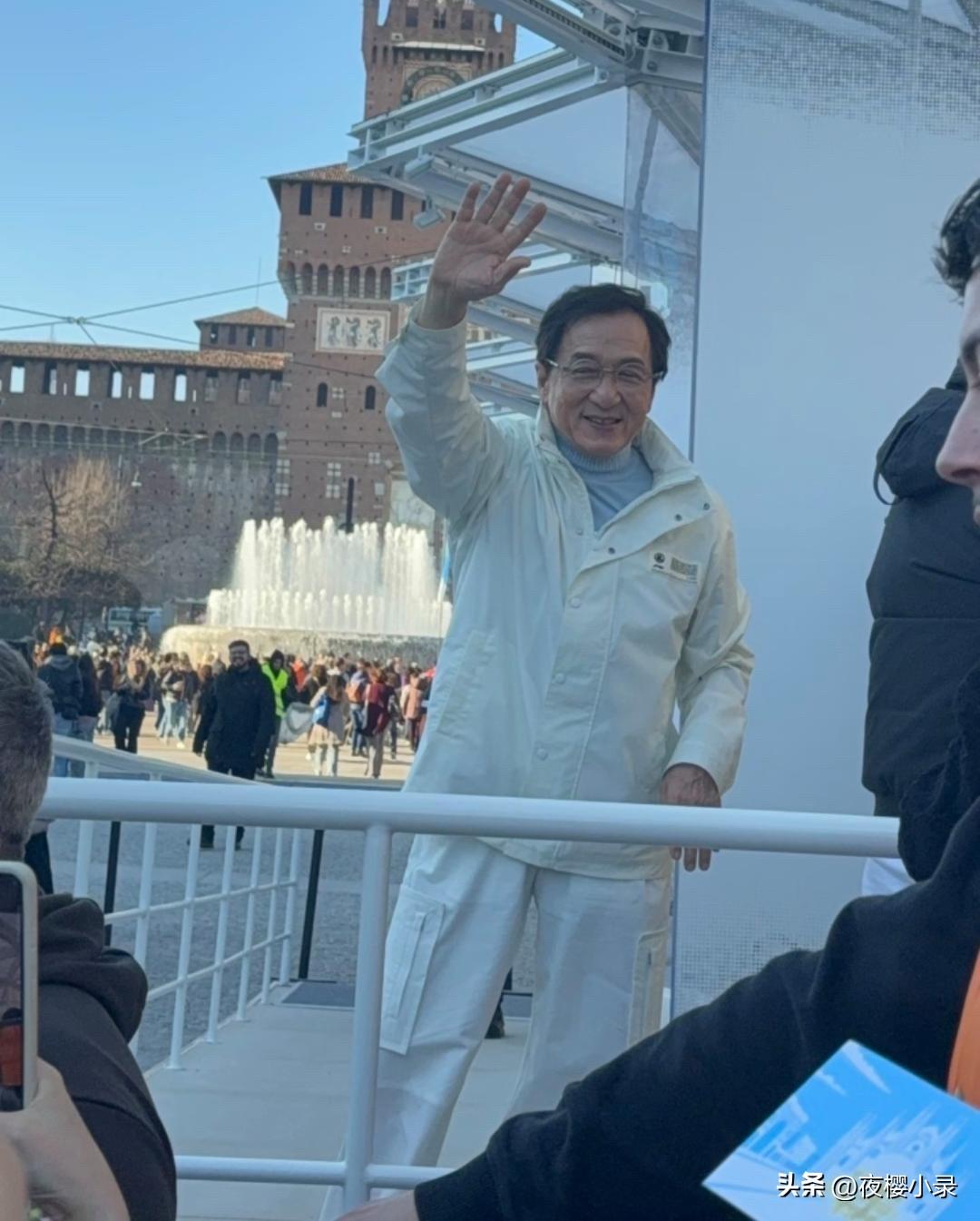 72岁成龙在米兰被偶遇，他穿着白色运动外套，面露慈祥笑容和遇到的粉丝打招呼，看起